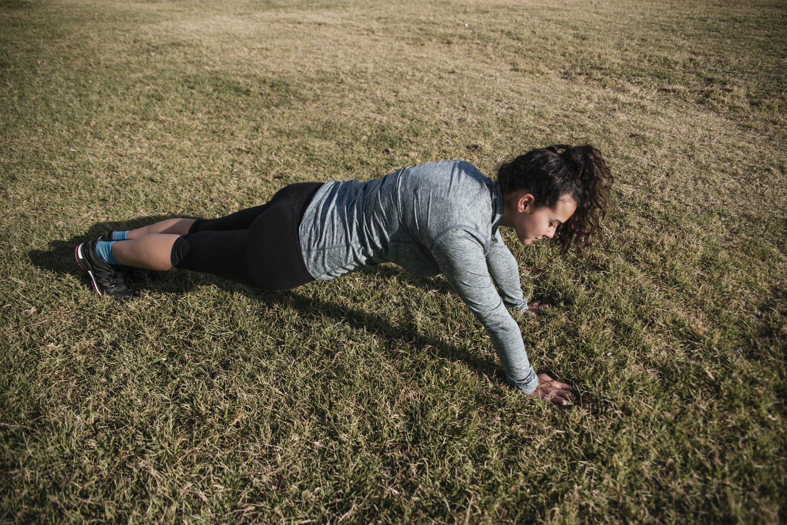 Stock photo of a caucasian woman doing push-ups in the grass. She is wearing sportswear.